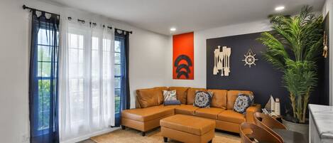 A modern living room with a sectional sofa, a dining area with a chair, and a large potted plant.