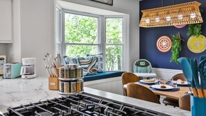 Et moderne køkken med gasblus, et vindue med udsigt til grøn natur, et spiseområde med bord dækket til to samt en hængende lampe.