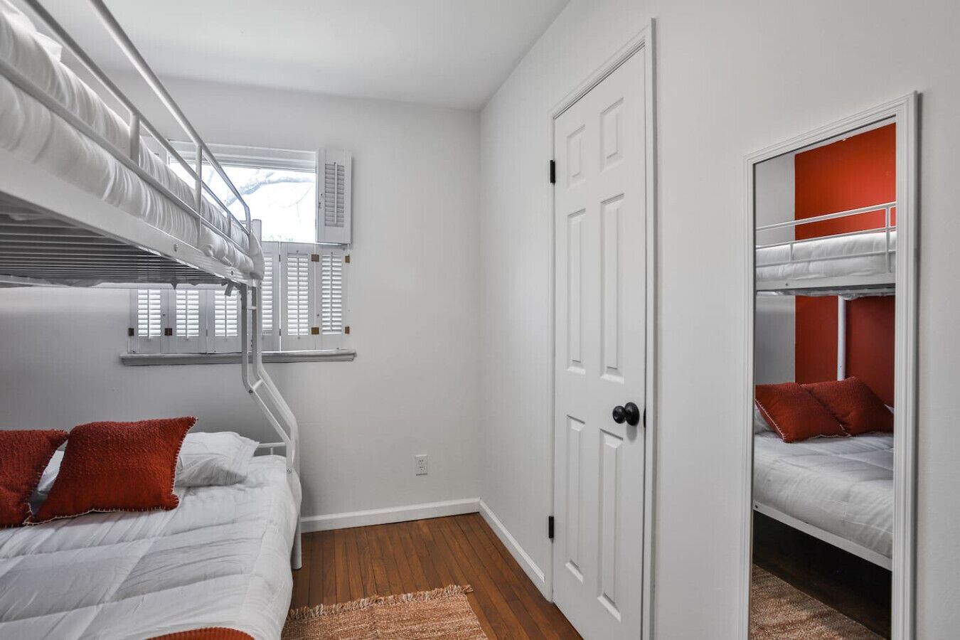 Habitación tipo dormitorio con literas, una ventana con persianas, una puerta y un espejo.