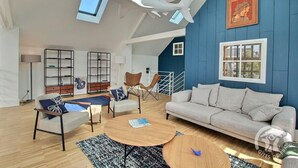 Ein geräumiges Wohnzimmer mit hoher Decke, einer blauen Akzentwand, einem modernen Sofa, einem Holztisch und einem Bücherregal.