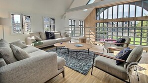 Ein geräumiges Wohnzimmer mit hoher Decke, großen Fenstern und Blick ins Freie.