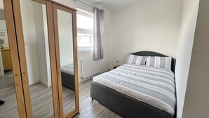 Un dormitorio con cama, armario, radiador y ventana con cortinas.