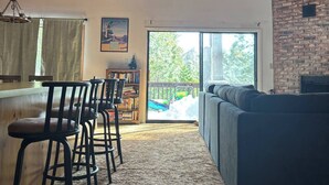 An interior with a high ceiling, wooden beams, a bar area with stools, a sofa, and a large window with a view of greenery. - The cozy cabin! (Twain Harte)