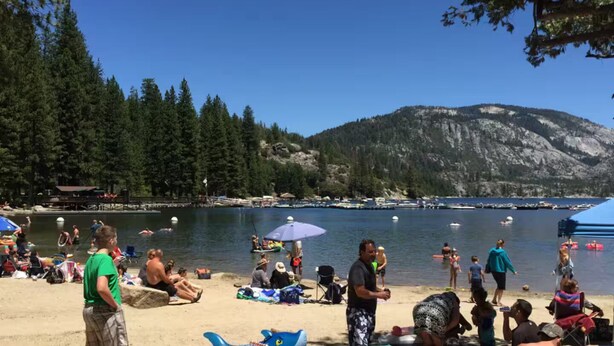 A beach with people relaxing and swimming, surrounded by trees and a mountain in the background. - The cozy cabin! (Twain Harte)