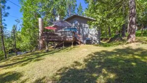 A cabin with a deck, surrounded by trees and a grassy yard. - The cozy cabin! (Twain Harte)