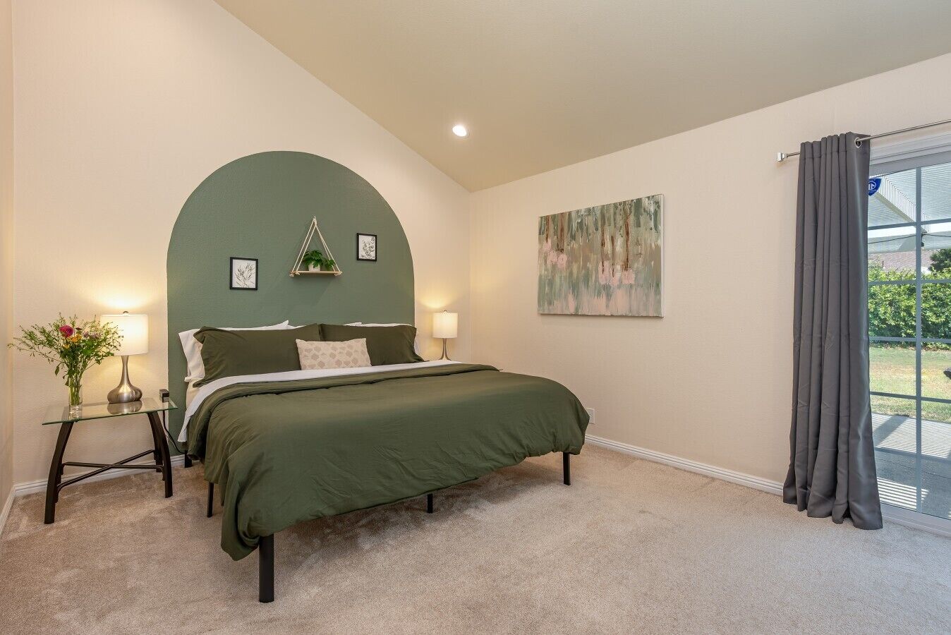 A bedroom with a bed, a nightstand, a lamp, a plant, and a painting.