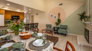 A dining area with a table set for four, surrounded by chairs. There is a kitchen in the background with wooden cabinets and a microwave. - Huge Backyard, Near Disney, Family Friendly, Quiet Neighborhood (Placentia)