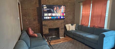 A living room with a large flat-screen TV mounted on a brick wall, a ceiling fan, and two sofas.