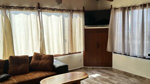 A cozy living room with a wooden ceiling, a sofa, a coffee table, and a green quilted bed. - Puesta de sol (Ixtapa)