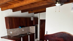 A compact bedroom with a bed, a wooden coffee table, a small seating area, and a kitchenette with a sink and cabinets. - Puesta de sol (Ixtapa)