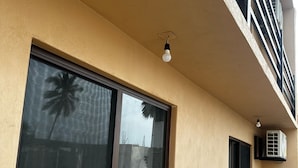 A building with a large window reflecting palm trees, a balcony with a railing, and an air conditioning unit mounted on the wall. - Puesta de sol (Ixtapa)