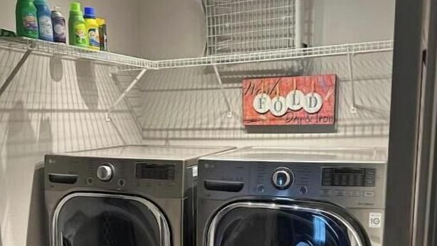 A laundry room with two stainless steel front-loading washers and dryers, a metal shelf with detergent bottles, and a sign above the dryers.