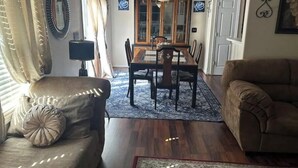 A living room with a sofa, a dining table with chairs, a patterned rug, and a chandelier.