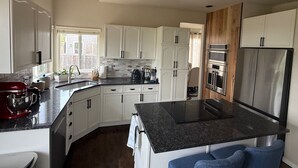 Une cuisine moderne avec des meubles blancs, un plan de travail en granit, des appareils électroménagers en acier inoxydable et une fenêtre laissant entrer la lumière naturelle.