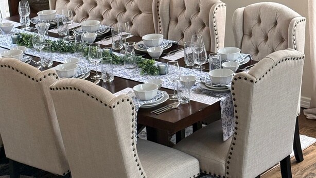 Une salle à manger avec une grande table dressée pour six personnes, entourée de chaises rembourrées dont les dossiers sont ornés de boutons.