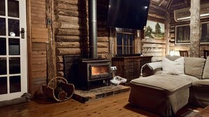 L’intérieur d’une cabane en rondins, avec un poêle à bois, un canapé et un tableau accroché au mur.