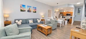 A modern living room with a sofa, armchairs, a coffee table, and a dining area with a table and chairs.
