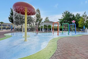 A water play area with a large water fountain, a gazebo, and colorful play structures.