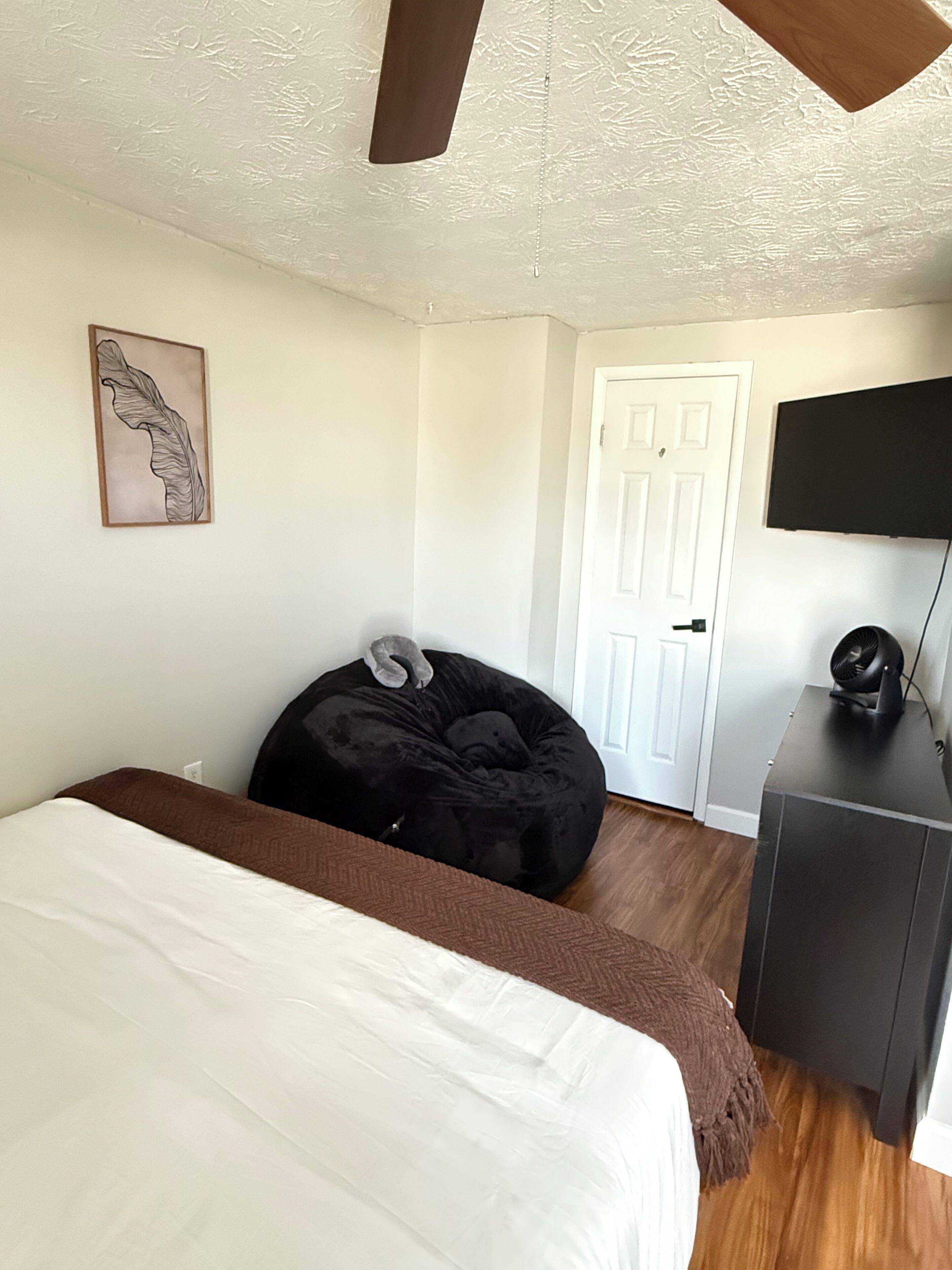 A bedroom with a bed, a bean bag chair, a TV, and a door.