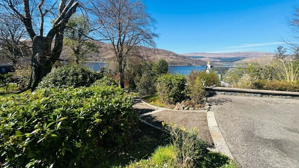 A scenic view of a lake with a clear sky, surrounded by trees and a gravel path leading to a house. - The Shack in Fort William (Fort William)