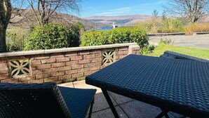 A patio with two wicker chairs and a table, overlooking a scenic landscape with hills and a body of water. - The Shack in Fort William (Fort William)