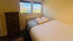 A bedroom with a bed, a dresser, a radiator, and a window with a view of hills. - The Shack in Fort William (Fort William)