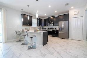 A modern kitchen with dark cabinets, stainless steel appliances, and a marble-tiled floor. - 6-Bedroom Retreat in Champions Gate (Four Corners)