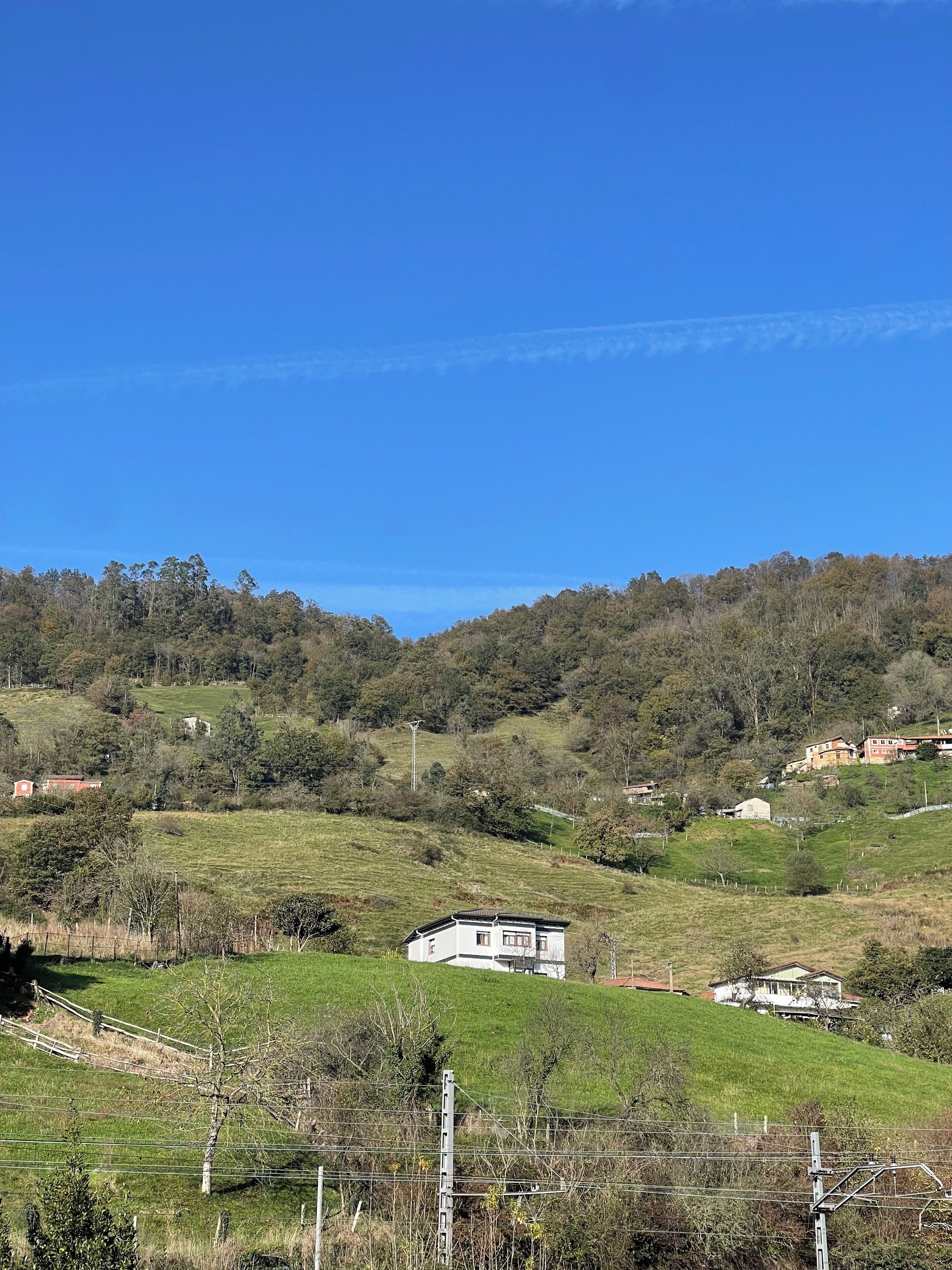 Paisaje rural con colinas ondulantes, casas dispersas y cielo azul despejado.