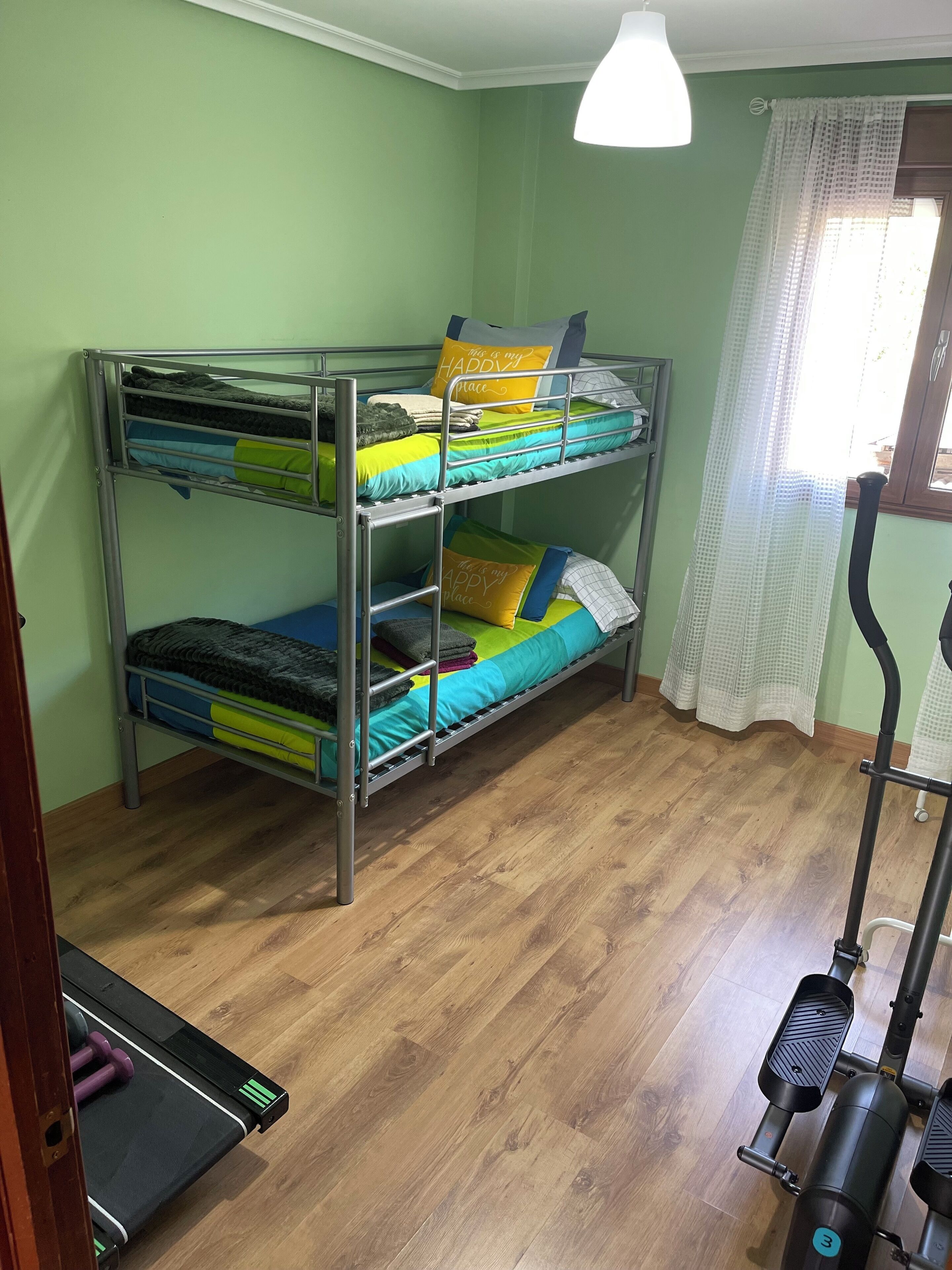 Ein Stockbett mit farbenfroher Bettwäsche, ein Laufband und ein Fenster mit Vorhängen.