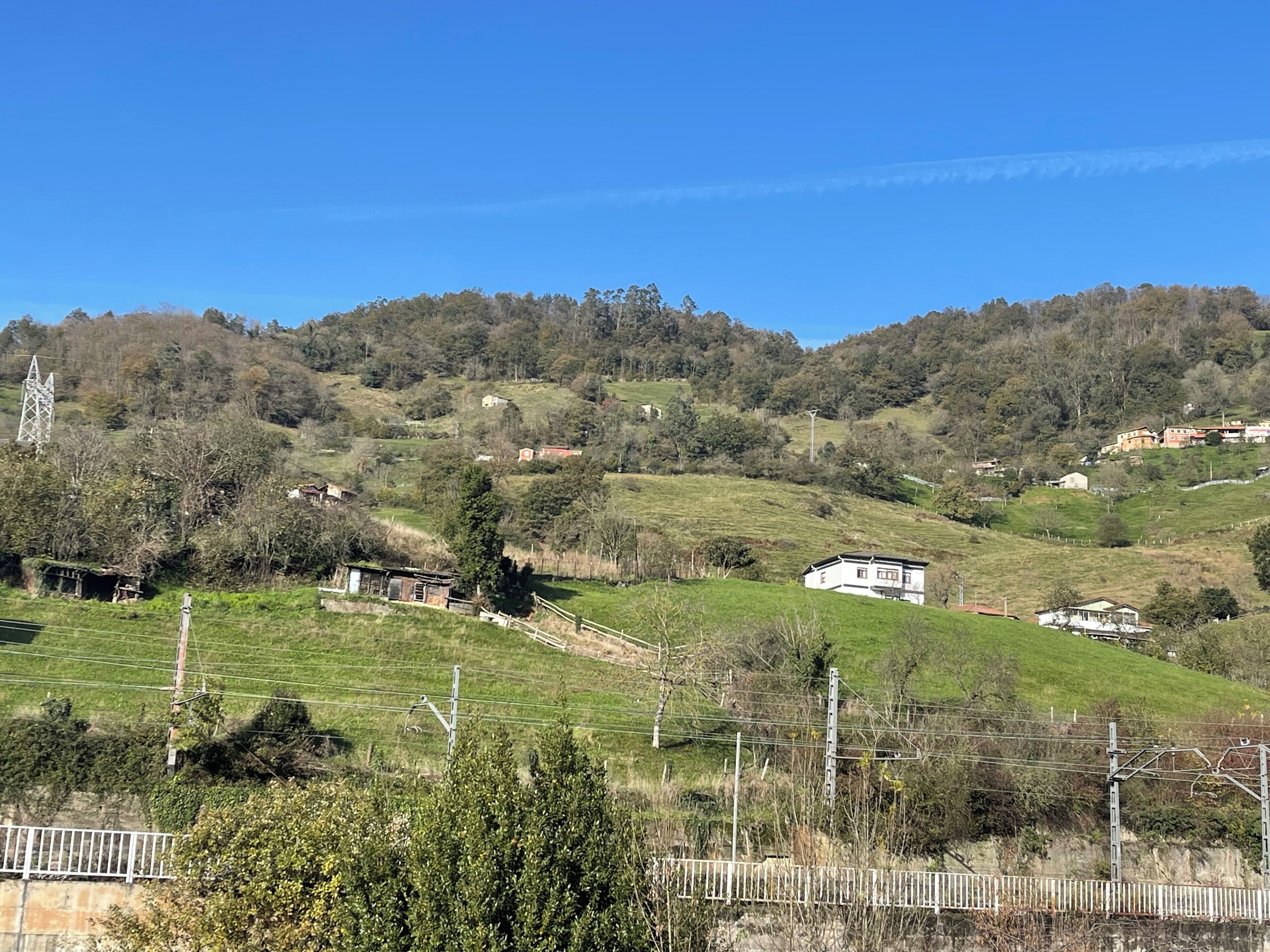 Un paysage rural caractérisé par des collines douces, des maisons dispersées et un ciel bleu dégagé.