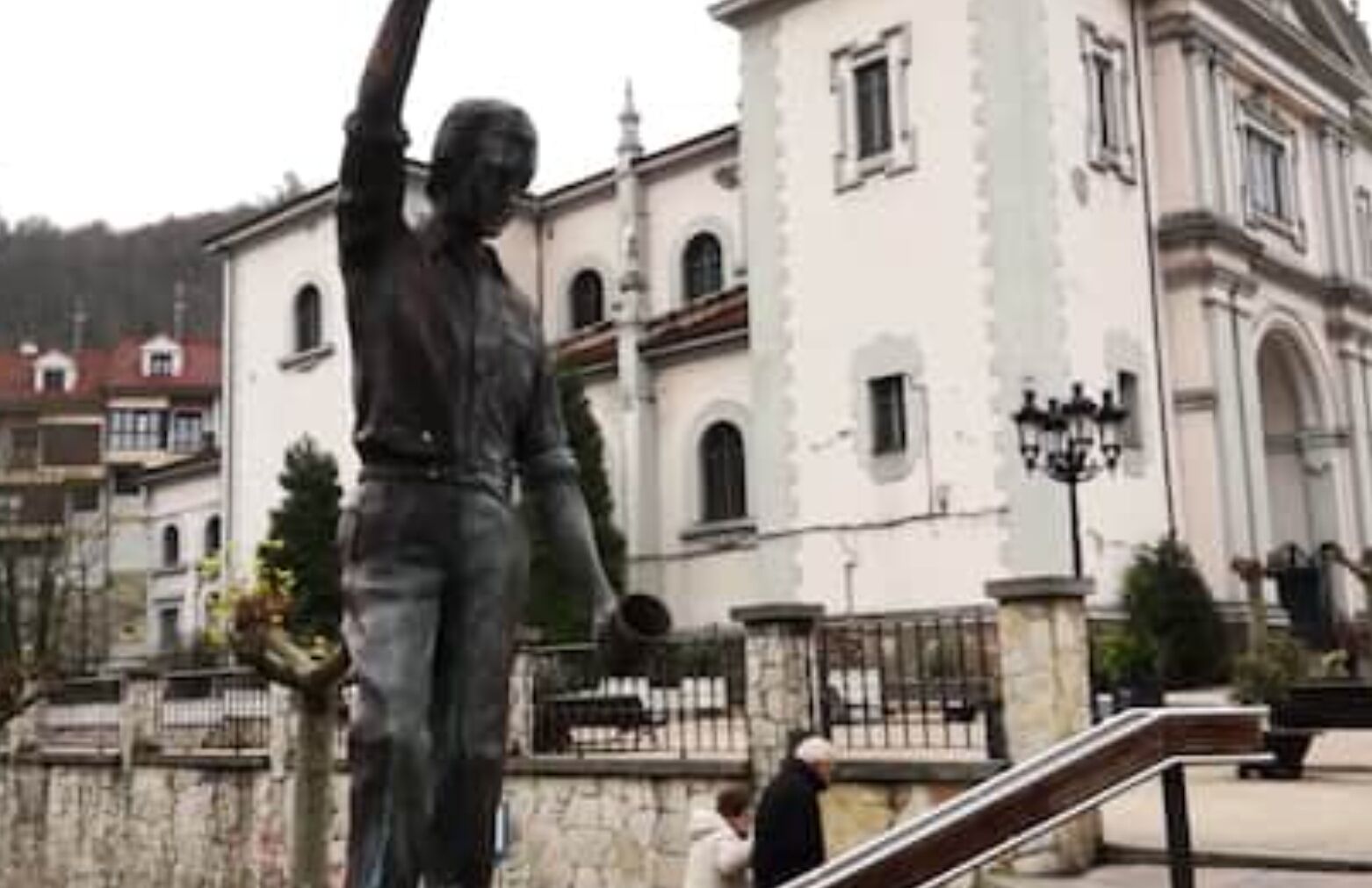 Une statue se trouve sur une place publique, avec un bâtiment en arrière-plan.