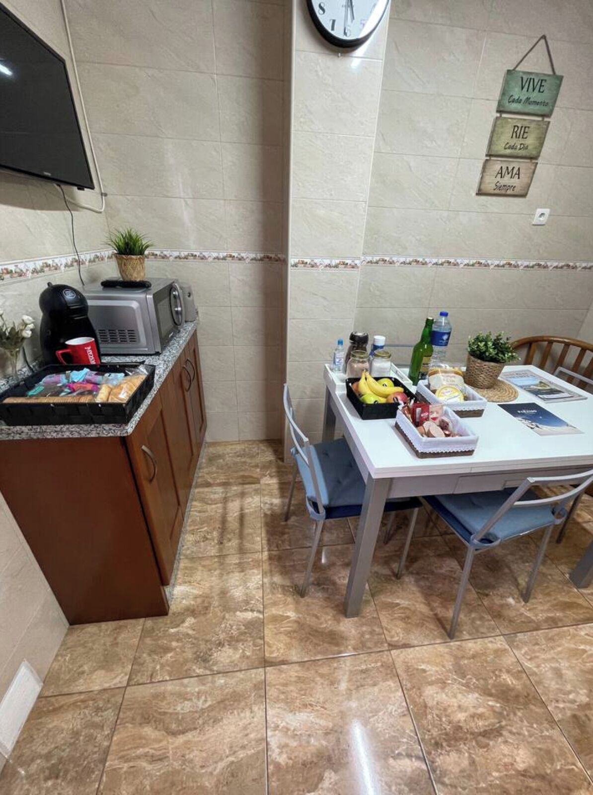 Una cocina compacta con comedor, cafetera, tostadora y un reloj en la pared.