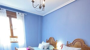 Una habitación con dos camas de madera, un candelabro y una ventana con cortinas.