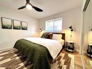 Een slaapkamer met een bed, een plafondventilator, een raam met zonwering en een vloerkleed.