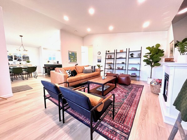 Een moderne woonkamer met een bank, salontafel en stoelen. Achtergrond toont een eethoek met een tafel en stoelen.