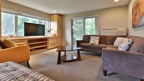 Un salon moderne avec un téléviseur à écran plat, un canapé marron, une table basse ronde et un tapis beige.