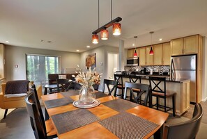 A modern kitchen with stainless steel appliances, wooden cabinets, and a dining area with a wooden table and chairs.