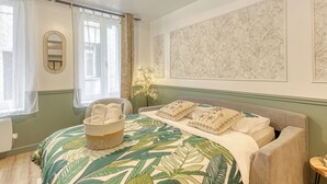 Un dormitorio con cama, mesita de noche, lámpara, ventana con cortinas y pared con estampado floral.