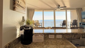 A kitchen with a view of the ocean, a ceiling fan, and a Keurig coffee maker.
