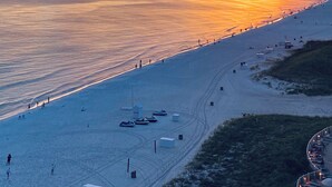A beach with a sunset, a pier, and a few boats.