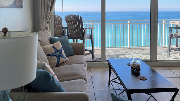 A living room with a sofa, chairs, a table, and a view of the ocean through large windows.