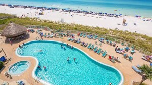 A pool area with multiple swimming pools, sun loungers, and a beach in the background.