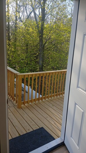 A wooden deck with a railing, a door, and a view of trees.