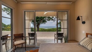 A bedroom with a large bed, a view of the sea through glass doors, and a seating area with chairs. - Spacious 5-bedroom villa 7 min drive from Pelada Beach (Nicoya)