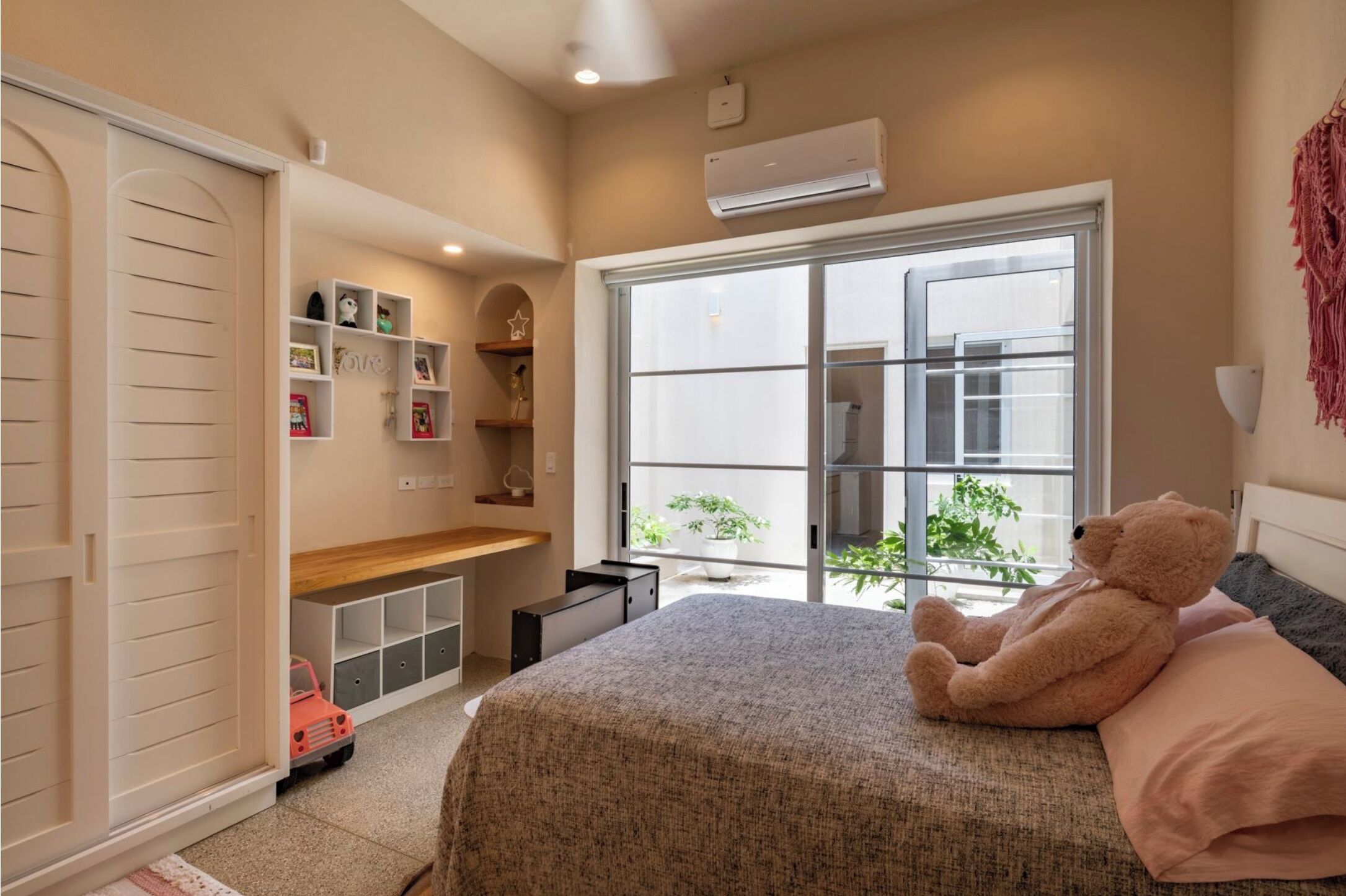A bedroom with a bed, a teddy bear, a window, and a closet.
