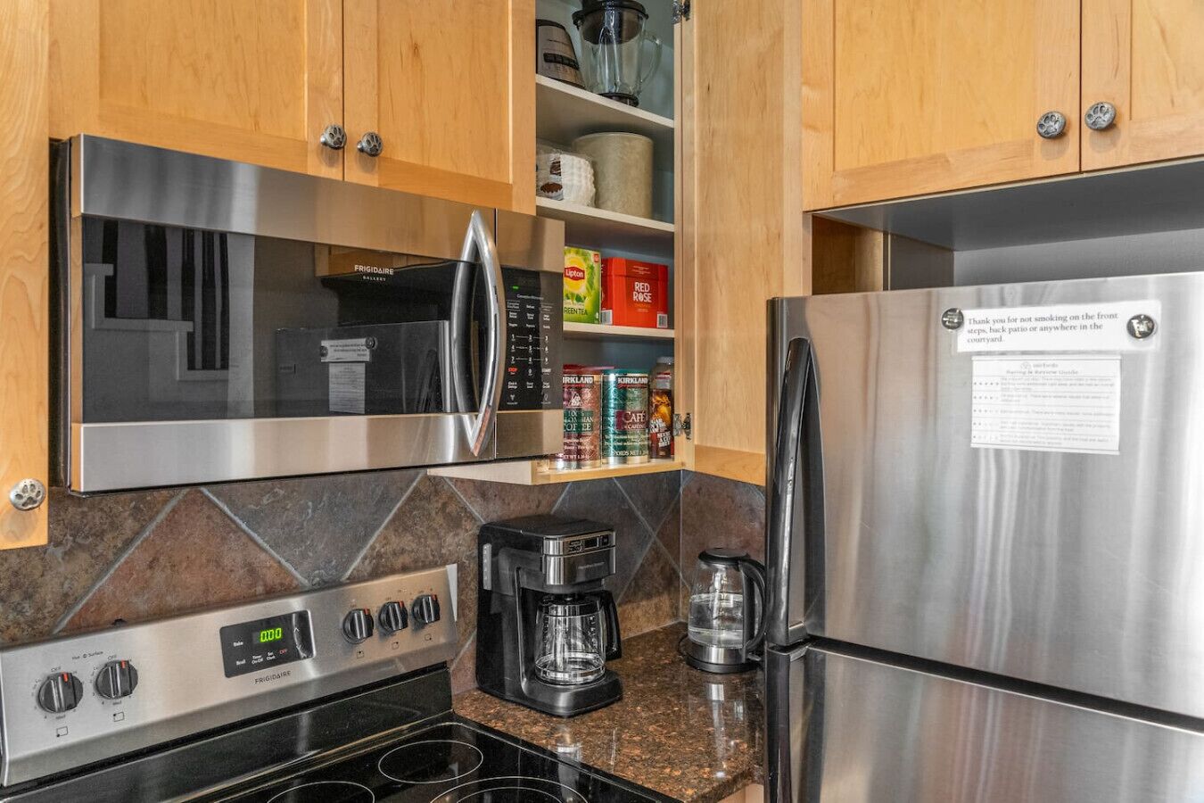 A modern kitchen with stainless steel appliances, including a refrigerator, microwave, and stove. There are cabinets with various items like coffee and tea, and a coffee maker on the counter.
