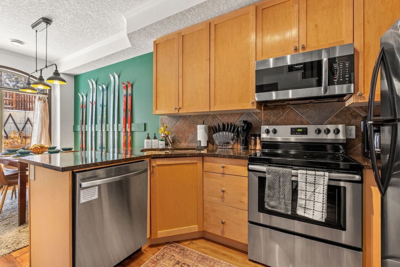 A modern kitchen with stainless steel appliances, wooden cabinets, and a green accent wall.