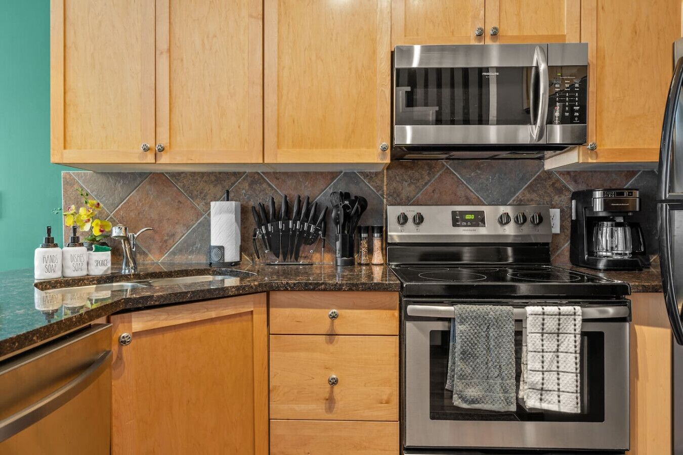 A modern kitchen with wooden cabinets, a stainless steel microwave, an oven, and a coffee maker.