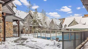 Un espacio exterior cubierto de nieve con piscina, muros de piedra y edificios de madera.