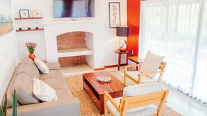 Un salon comprenant un canapé, des fauteuils, une table basse, une cheminée, un téléviseur et des œuvres d’art accrochées aux murs.